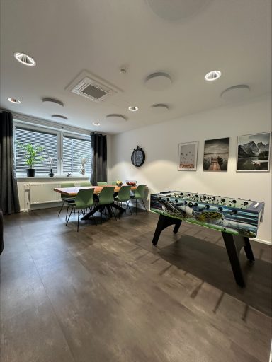Moderner Besprechungsraum mit einem großen Tisch und bunten Stühlen, Fenster mit Tageslicht.