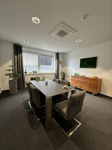 Moderne Büroumgebung mit Tisch, Stühlen, Pflanzen und einem dekorativen Sideboard.