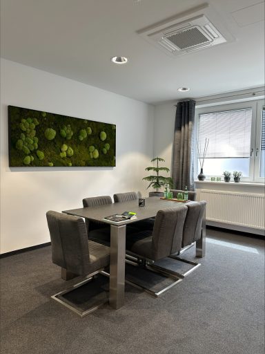 Moderne Esszimmer mit einem Tisch, Stühlen und einer grünen Wanddekoration.